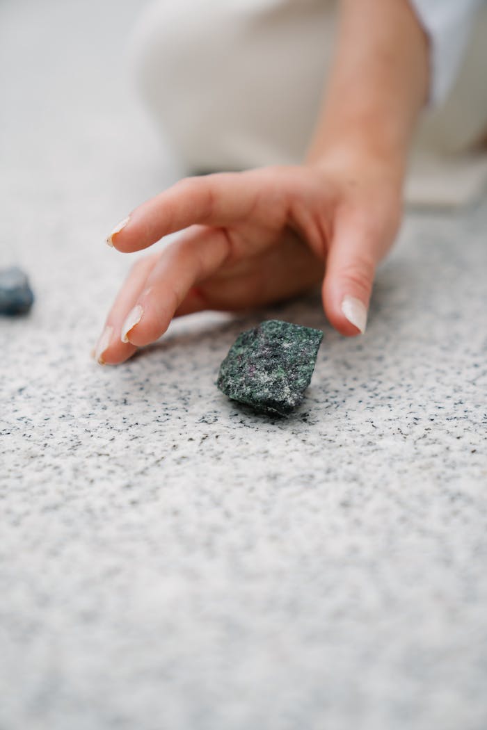 Hand gently touching a dark stone on a granite surface, evoking a sense of connection with nature.
